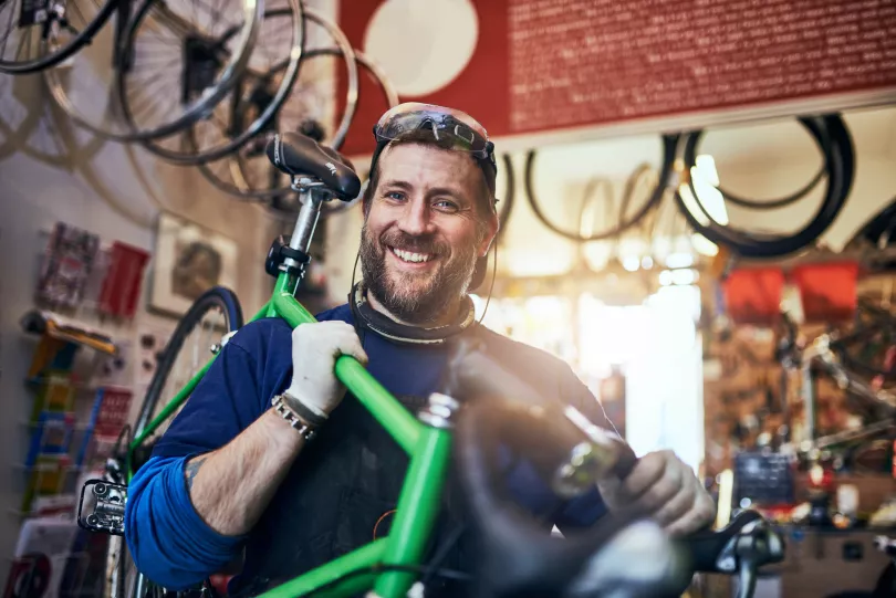 Een man met een fiets op zijn schouder glimlacht naar de camera